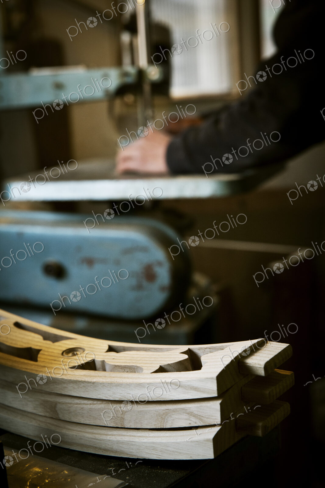 A man working in a furniture maker’s workshop using a mechanical saw. Wooden chair…