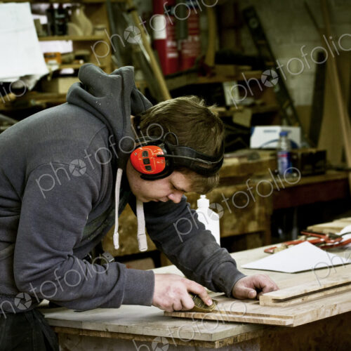 A man working in a furniture maker's workshop wearing ear defenders and using a sharp… A man working in a furniture maker's workshop wearing ear defenders and using a sharp…