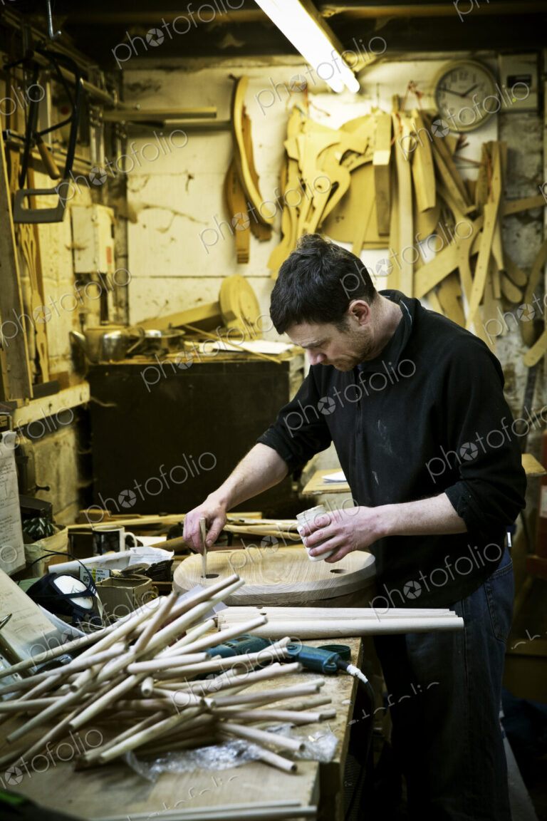 A man working in a furniture maker's workshop. Chairlegs on the bench.