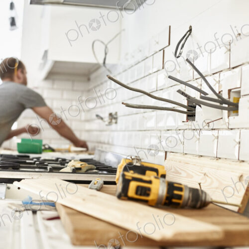 A man working in a new kitchen, a tiler applying tiles to the wall behind the cooker. A man working in a new kitchen, a tiler applying tiles to the wall behind the cooker.
