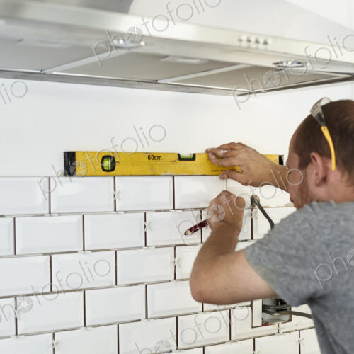 A man working in a new kitchen, a tiler applying tiles to the wall behind the cooker. A man working in a new kitchen, a tiler applying tiles to the wall behind the cooker.