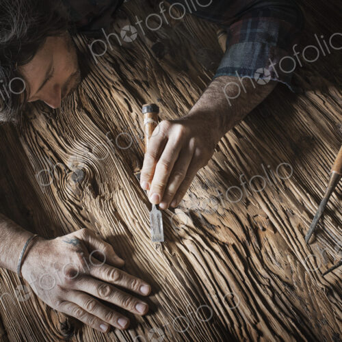 A man working in a reclaimed lumber yard workshop. Holding tools and sanding knotted…