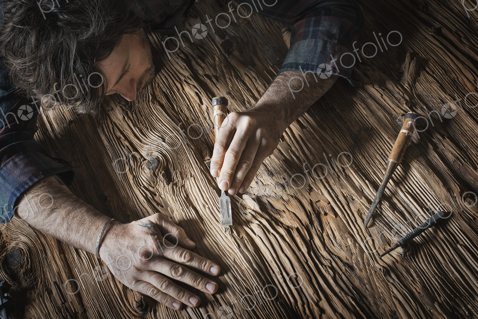 A man working in a reclaimed lumber yard workshop. Holding tools and sanding knotted…