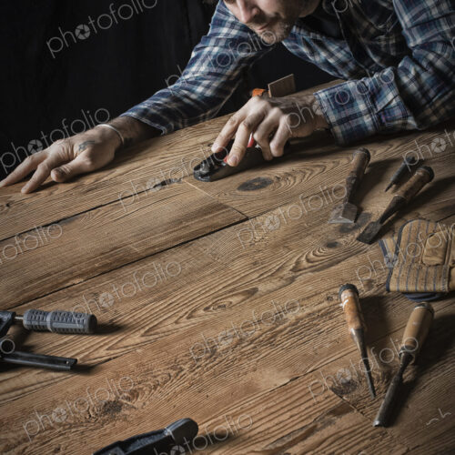 A man working in a reclaimed lumber yard workshop. Holding tools and sanding knotted…