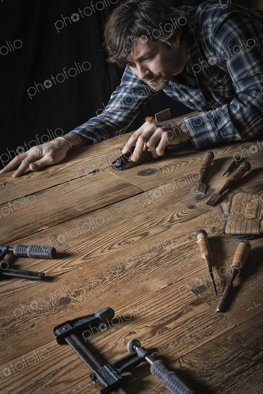 A man working in a reclaimed lumber yard workshop. Holding tools and sanding knotted…