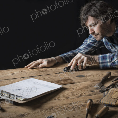 A man working in a reclaimed lumber yard workshop. Holding tools and sanding knotted…