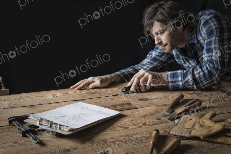 A man working in a reclaimed lumber yard workshop. Holding tools and sanding knotted…
