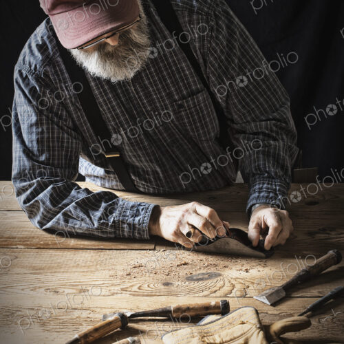 A man working in a reclaimed lumber yard workshop. Holding tools and sanding knotted…