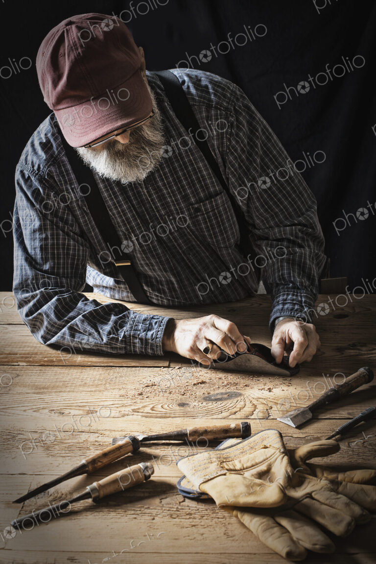 A man working in a reclaimed lumber yard workshop. Holding tools and sanding knotted…