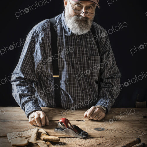A man working in a reclaimed lumber yard workshop. Holding tools and working on a…