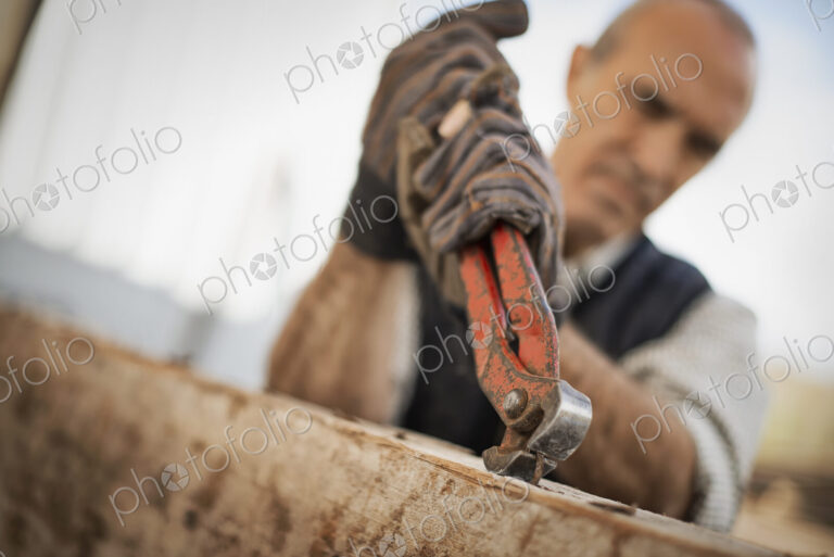 A man working in a reclaimed timber yard. Using a tool to remove metals from a…