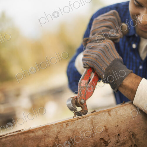 A man working in a reclaimed timber yard. Using a tool to remove metals from a… A man working in a reclaimed timber yard. Using a tool to remove metals from a…