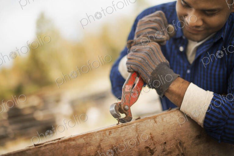 A man working in a reclaimed timber yard. Using a tool to remove metals from a…
