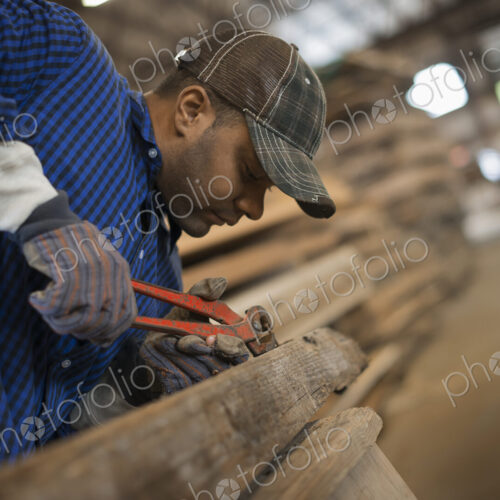 A man working in a reclaimed timber yard. Using a tool to remove metals from a…