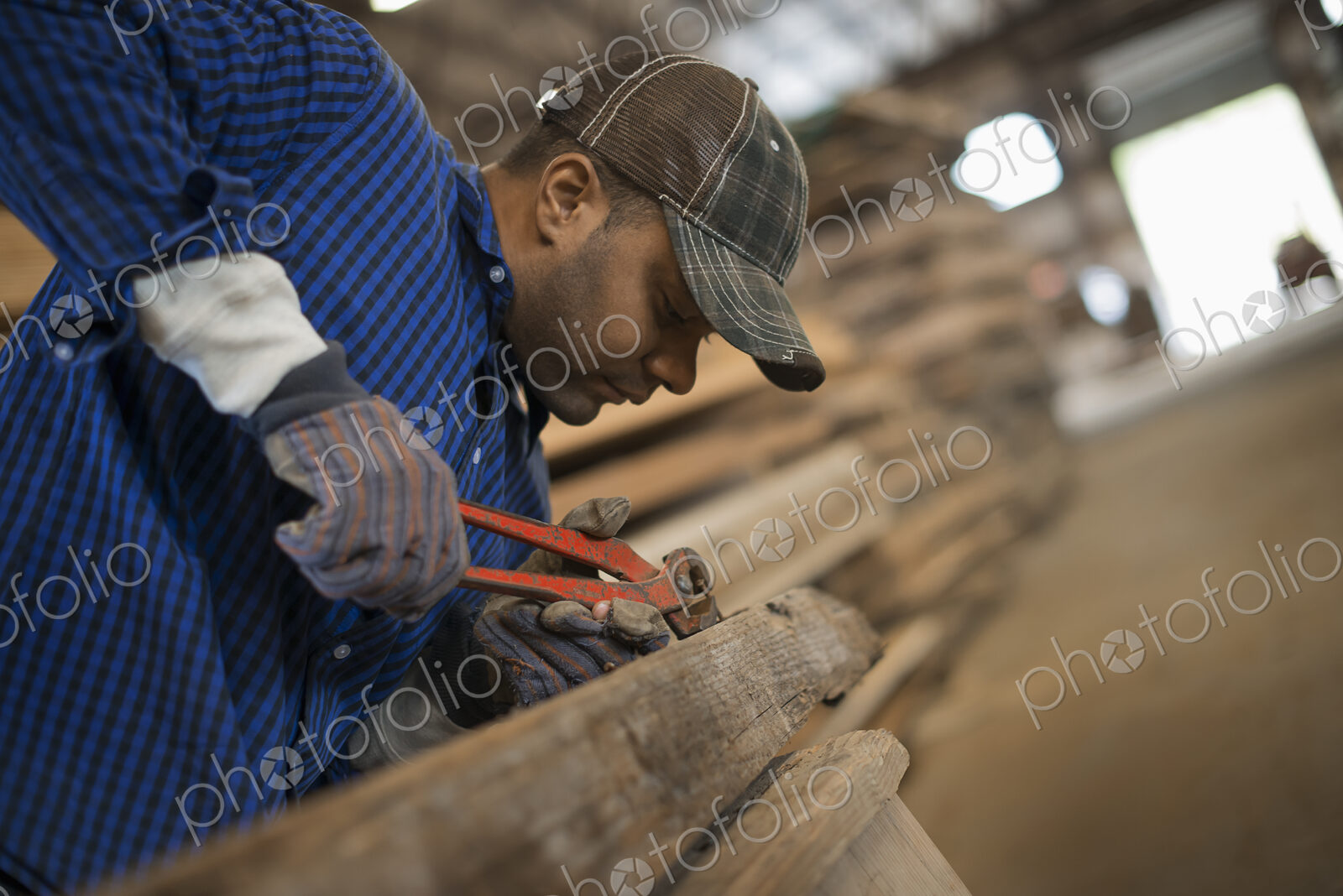 A man working in a reclaimed timber yard. Using a tool to remove metals from a…