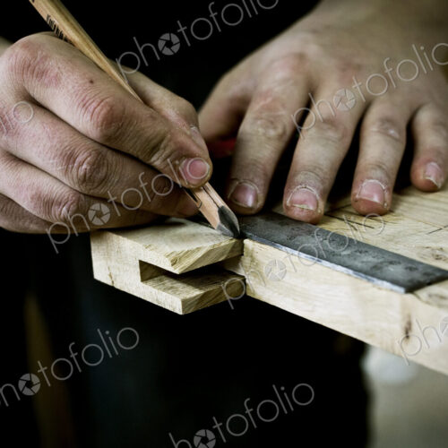 A man working on wood, measuring a joint or corner with a ruler and pencil. A man working on wood, measuring a joint or corner with a ruler and pencil.
