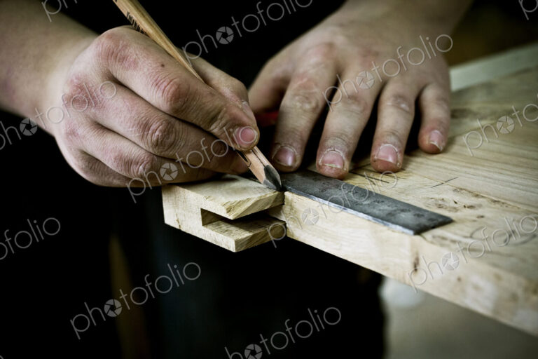 A man working on wood, measuring a joint or corner with a ruler and pencil.