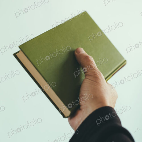 A man's hand holding an old green hardback book. A man's hand holding an old green hardback book.