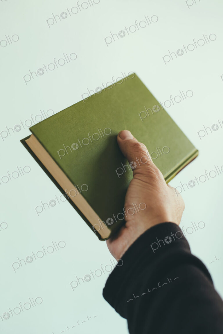 A man's hand holding an old green hardback book.