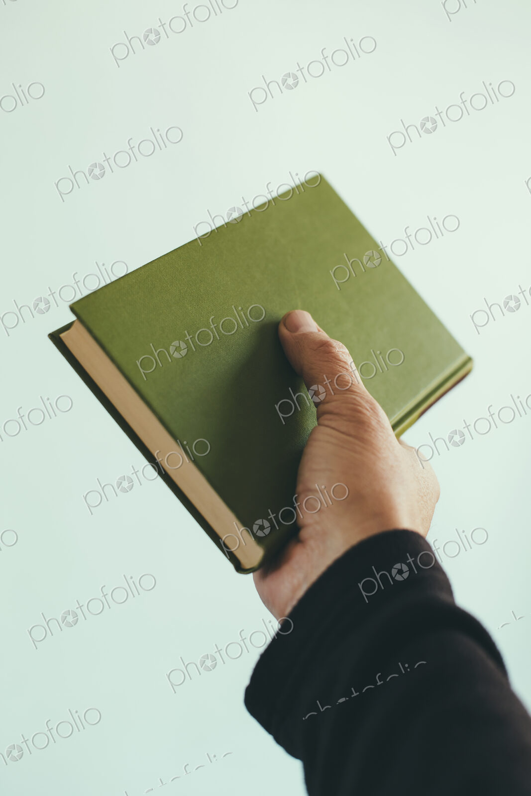 A man’s hand holding an old green hardback book.