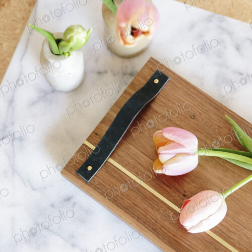 A marble slab with two vases and pink tulips and a wooden board with handle.
