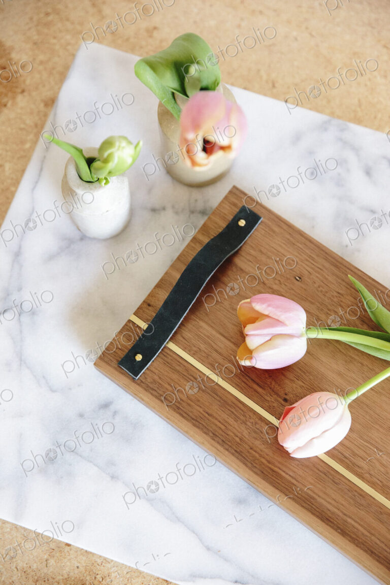 A marble slab with two vases and pink tulips and a wooden board with handle.