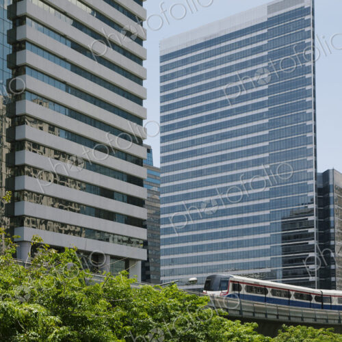 A mass transit train on an elevated track passes modern glass buildings in the central…