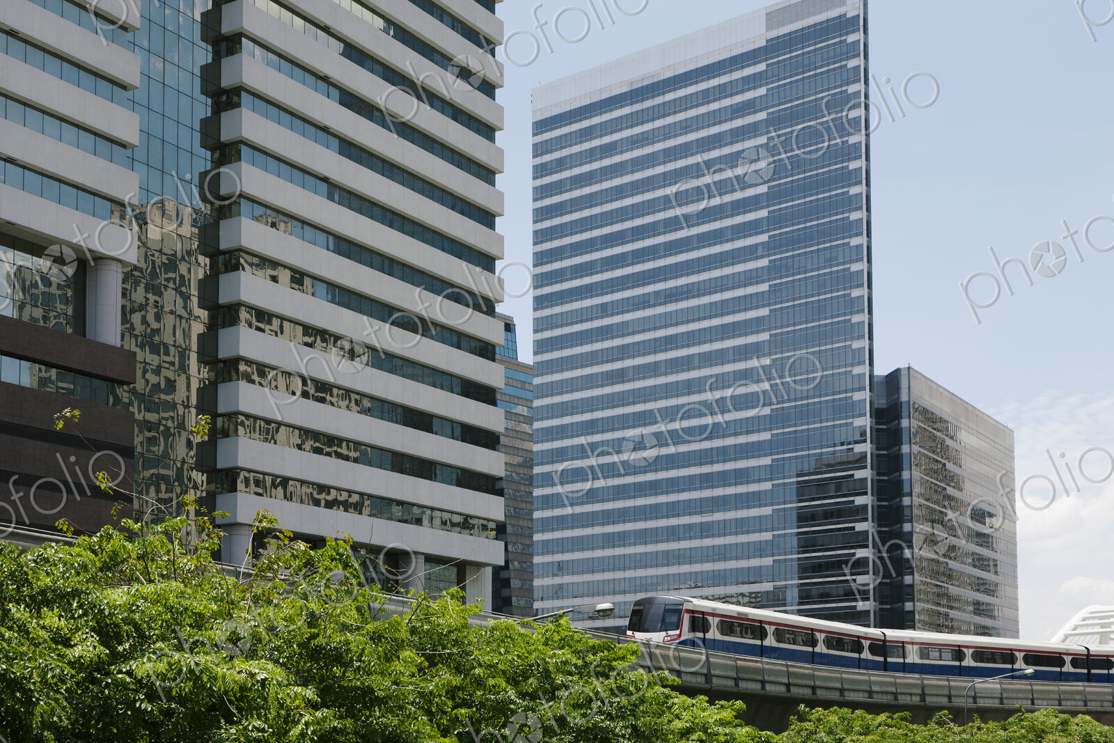 A mass transit train on an elevated track passes modern glass buildings in the central…