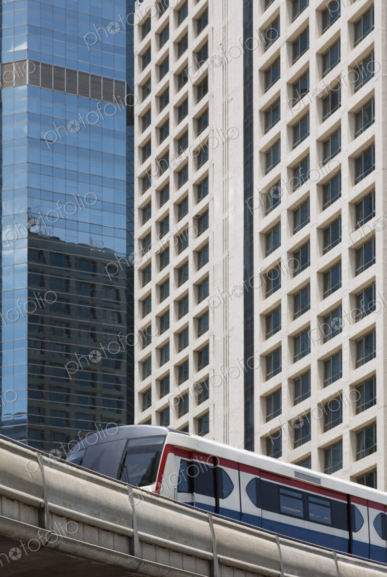 A mass transit train on an elevated track passing modern buildings in the central…