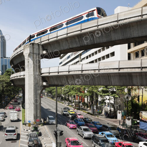 A mass transit train travelling on an elevated track above a busy city road in Bangkok.