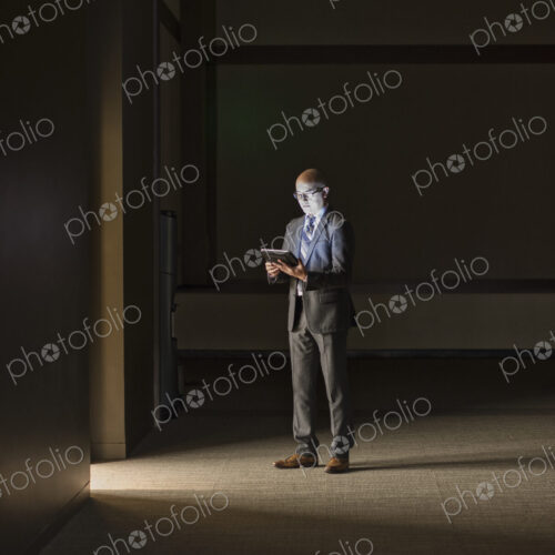 A mature Asian businessman standing in shadows in an office building, looking at a… A mature Asian businessman standing in shadows in an office building, looking at a…
