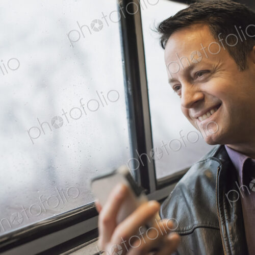 A mature man sitting at a window seat on a train, holding his mobile phone. Smiling…