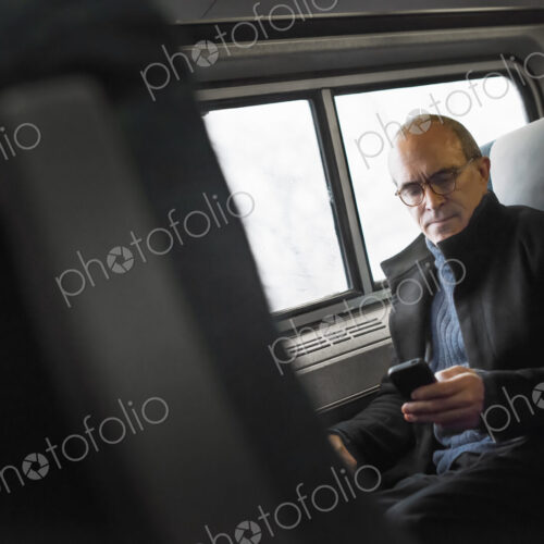 A mature man sitting by a window in a train carriage, using his mobile phone, keeping… A mature man sitting by a window in a train carriage, using his mobile phone, keeping…