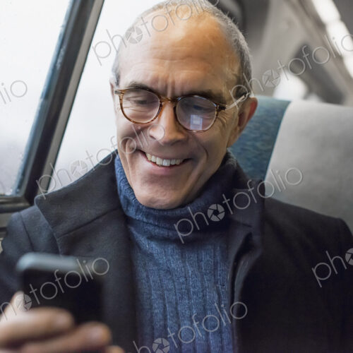A mature man sitting by a window in a train carriage, using his mobile phone, keeping… A mature man sitting by a window in a train carriage, using his mobile phone, keeping…