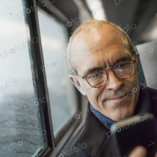 A mature man sitting by a window in a train carriage, using his mobile phone, keeping… A mature man sitting by a window in a train carriage, using his mobile phone, keeping…