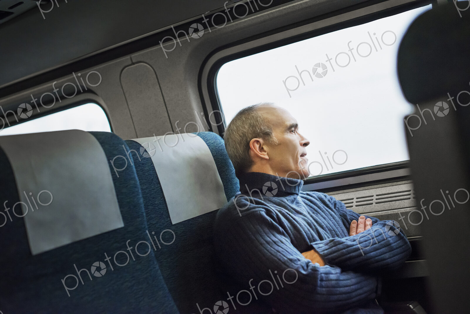 A mature man sitting in a window seat on a train journey, looking out into the distance.