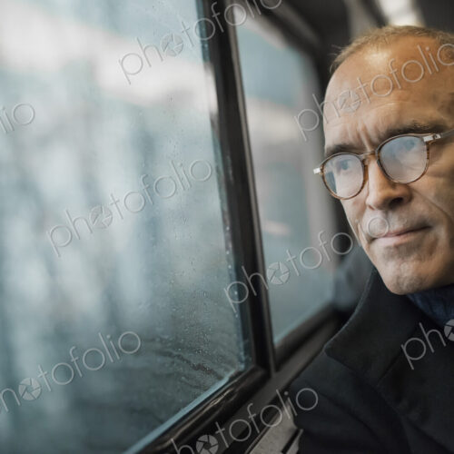 A mature man sitting in a window seat on a train journey, looking out into the distance. A mature man sitting in a window seat on a train journey, looking out into the distance.