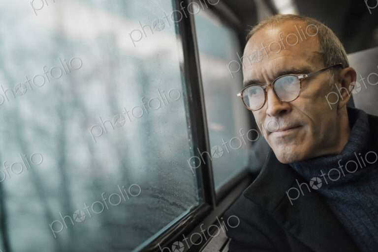 A mature man sitting in a window seat on a train journey, looking out into the distance.