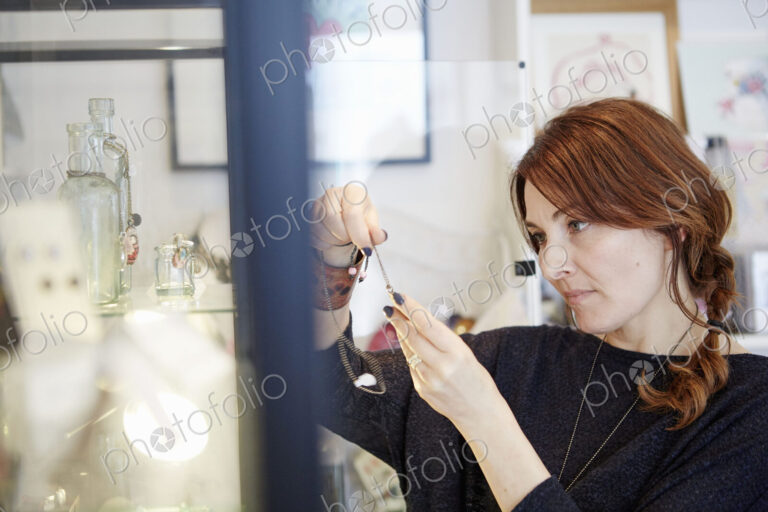 A mature woman holding a piece of jewellery in a shop