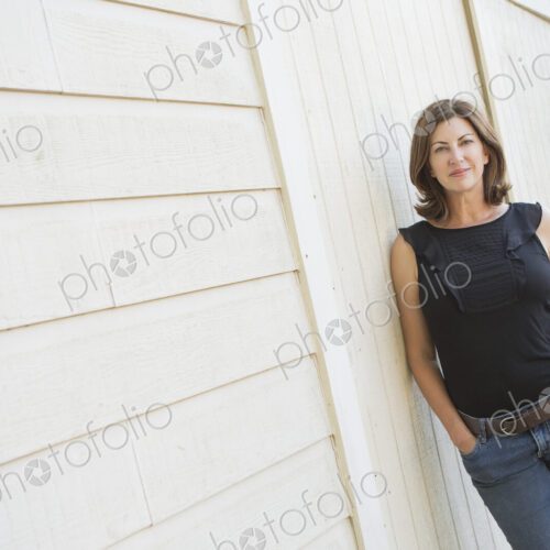A mature woman in a sleeveless shirt with shoulder length brunette hair, hands in her…