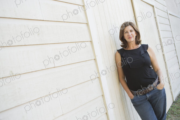A mature woman in a sleeveless shirt with shoulder length brunette hair, hands in her…