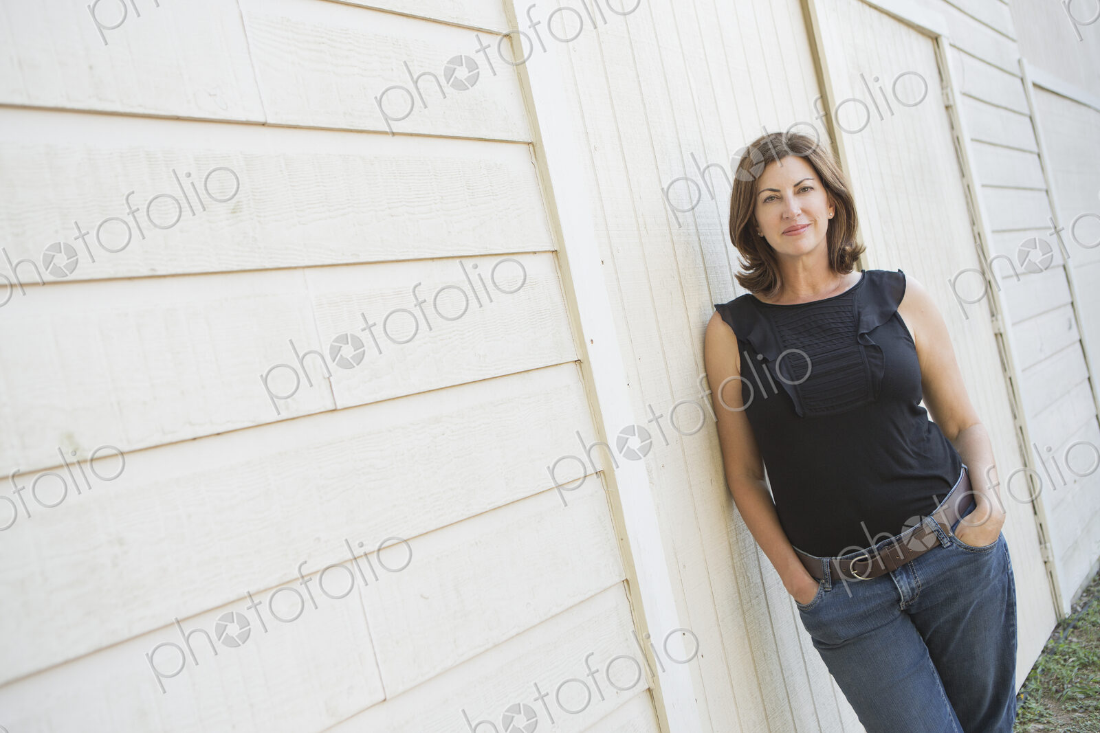 A mature woman in a sleeveless shirt with shoulder length brunette hair, hands in her…