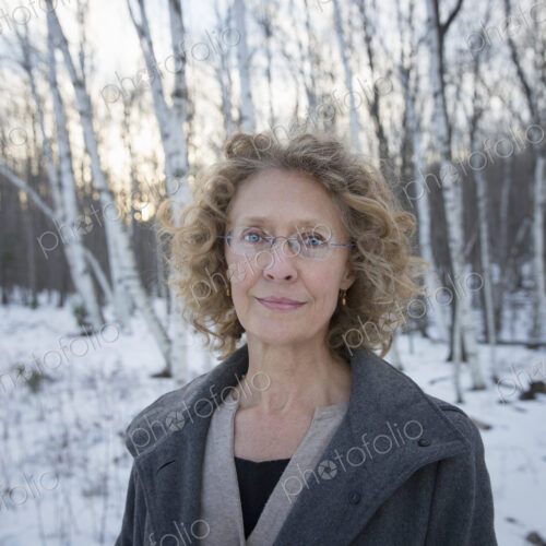 A mature woman with curly read hair, wearing a coat. Standing on a snowy path through… A mature woman with curly read hair, wearing a coat. Standing on a snowy path through…