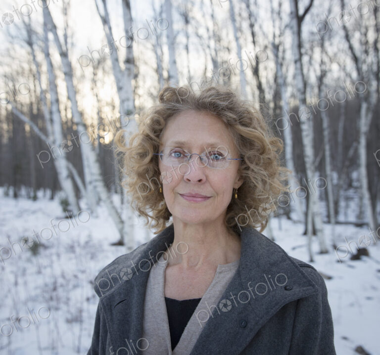 A mature woman with curly read hair, wearing a coat. Standing on a snowy path through…