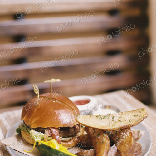 A meal, a hamburger in a bun, potato fries and a gherkin. A meal, a hamburger in a bun, potato fries and a gherkin.