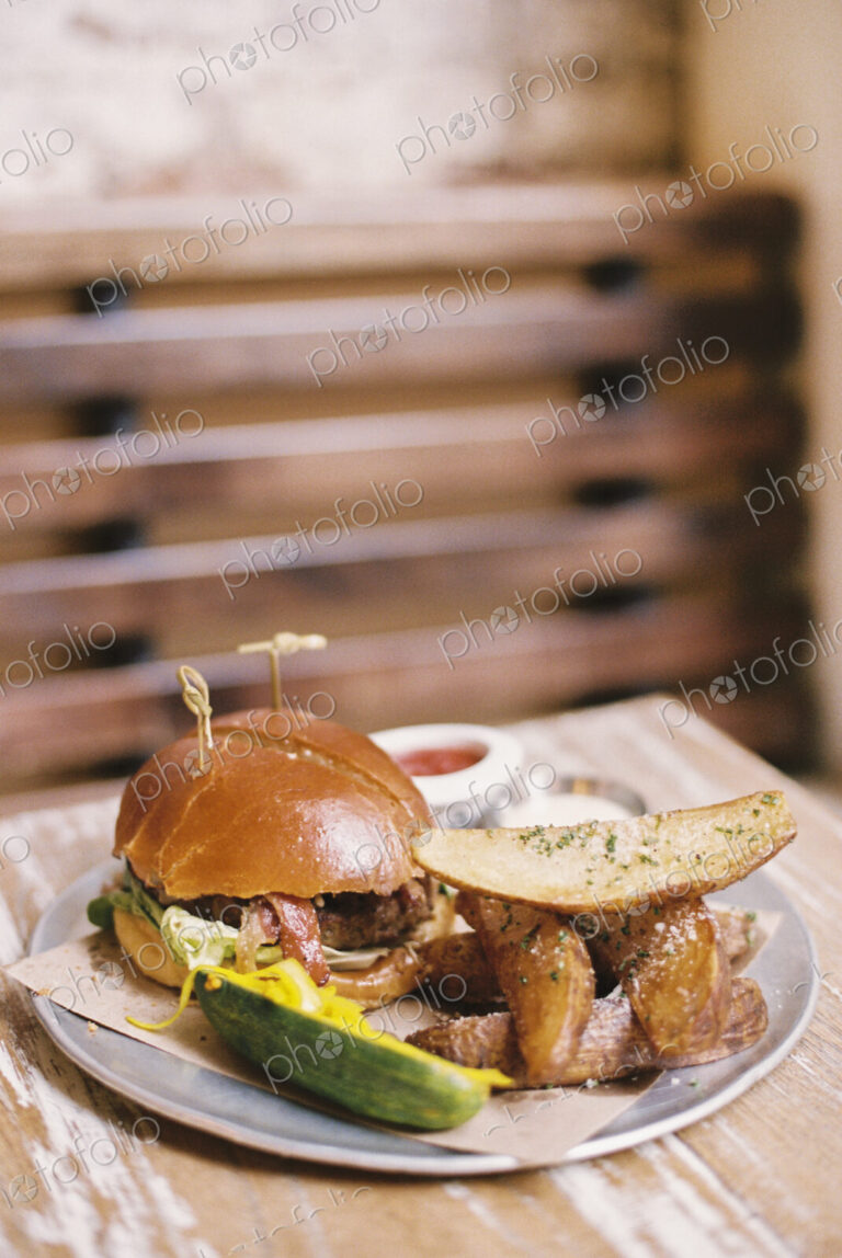 A meal, a hamburger in a bun, potato fries and a gherkin.