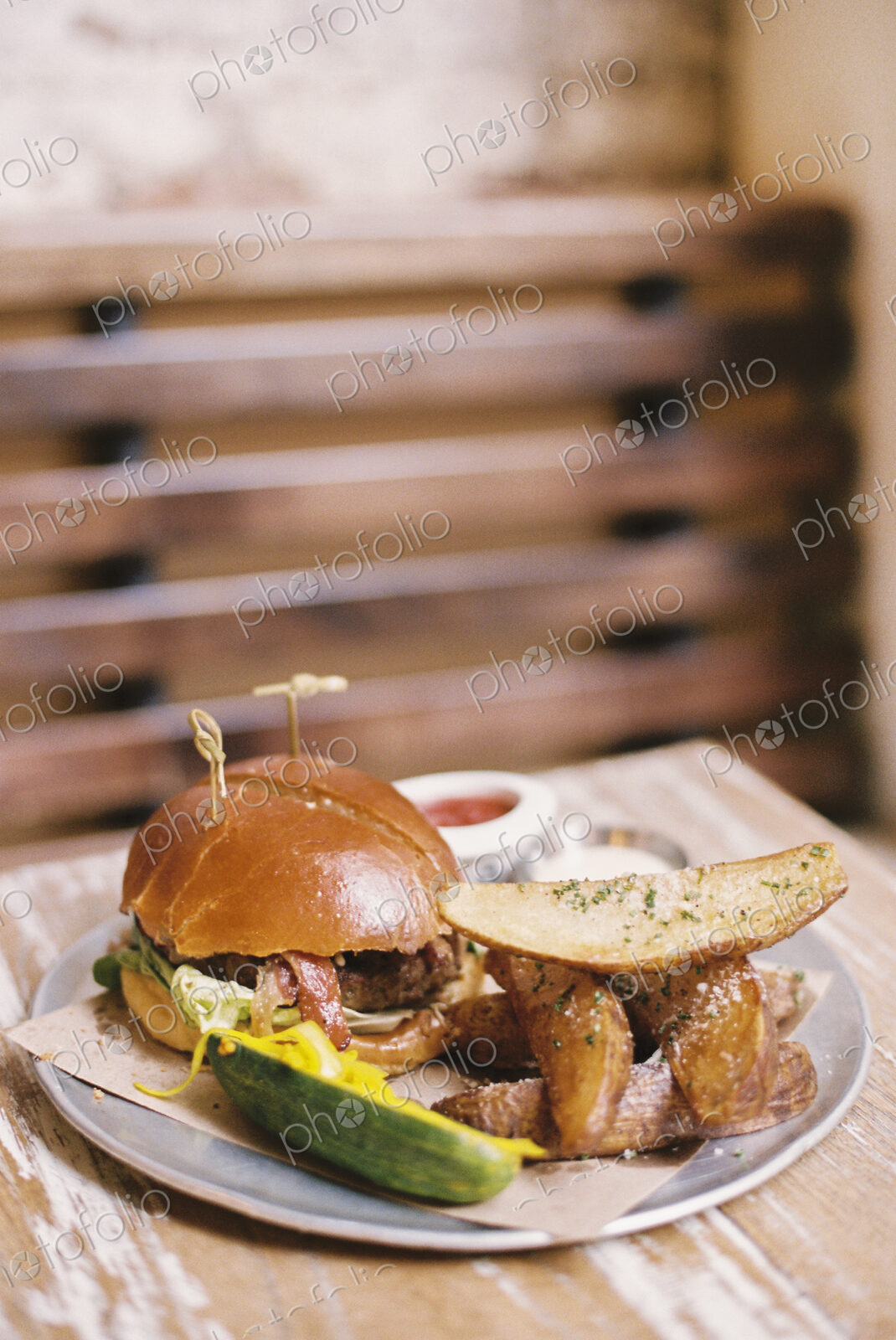 A meal, a hamburger in a bun, potato fries and a gherkin.