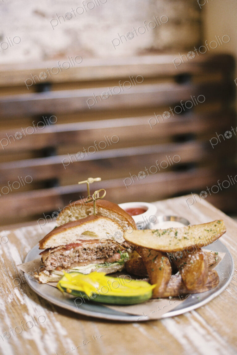 A meal, a hamburger in a bun, potato fries and a gherkin.