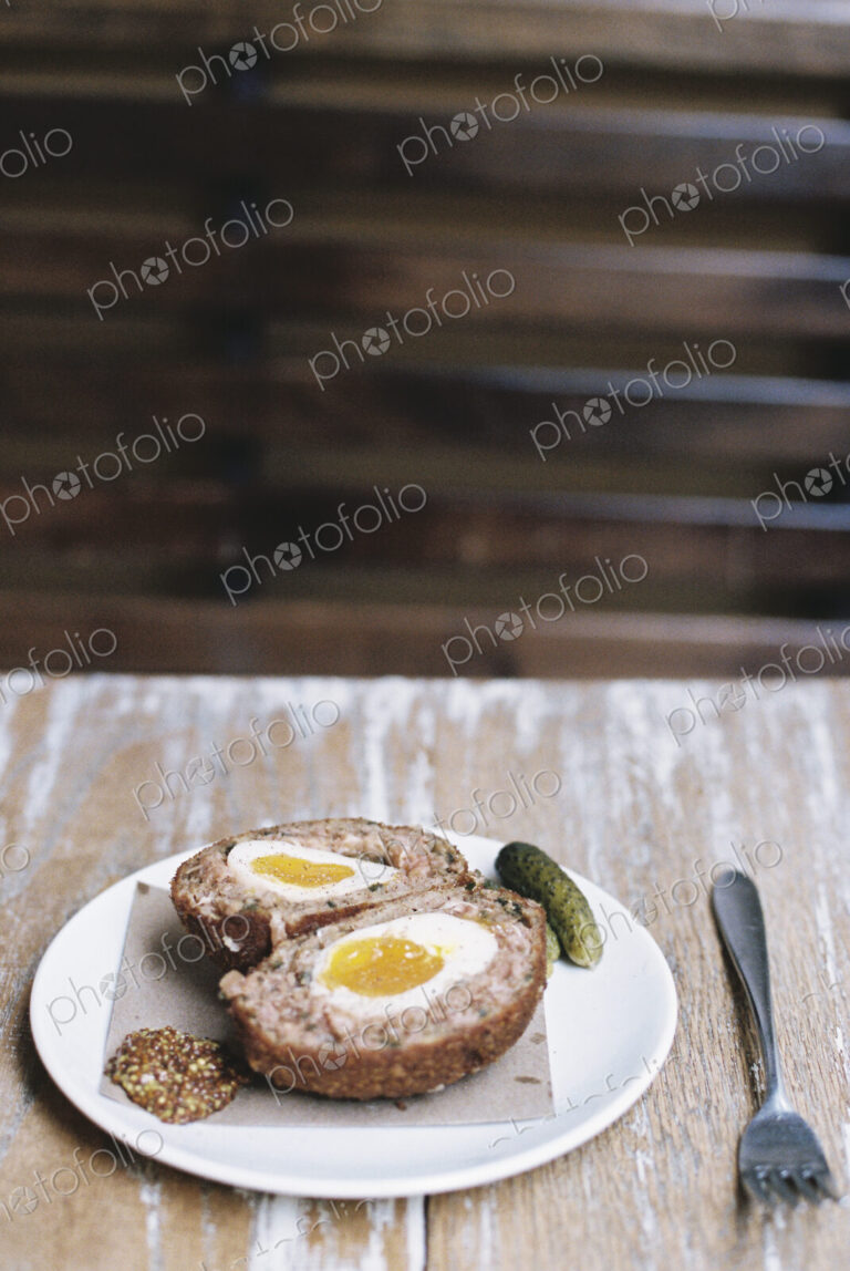 A meal on a plate, a scotch egg cut in half with garnishes.