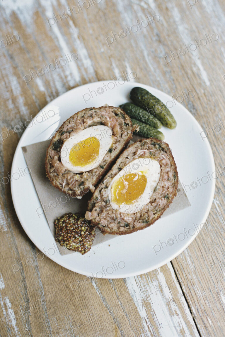 A meal on a plate, a scotch egg cut in half with garnishes.